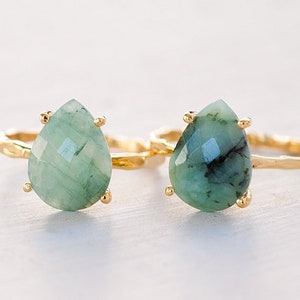 May include: Two gold rings with teardrop-shaped green gemstone settings. The rings have a twisted band design.