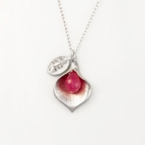May include: A silver necklace with a delicate flower pendant. The flower is open and holds a pink gemstone in the center. A small leaf with the word "love" engraved on it hangs from the flower.