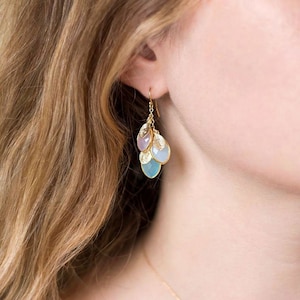 May include: Gold dangle earrings with a cluster of light blue, lavender, and white gemstone drops. Each gemstone is shaped like a teardrop and is accented with gold leaf charms.