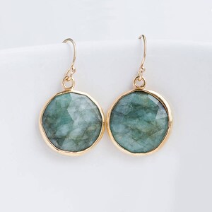 May include: A pair of gold earrings with round green gemstone drops. The earrings have a simple, elegant design.