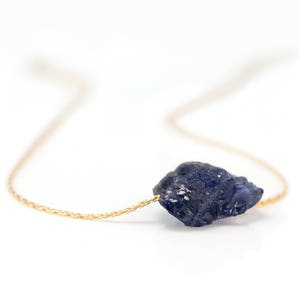 May include: A delicate gold chain necklace with a raw, dark blue kyanite gemstone pendant.