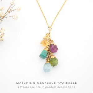 May include: Gold chain necklace with a cluster of five different colored gemstone pendants. The gemstones are a light orange, purple, turquoise, green, and light blue.