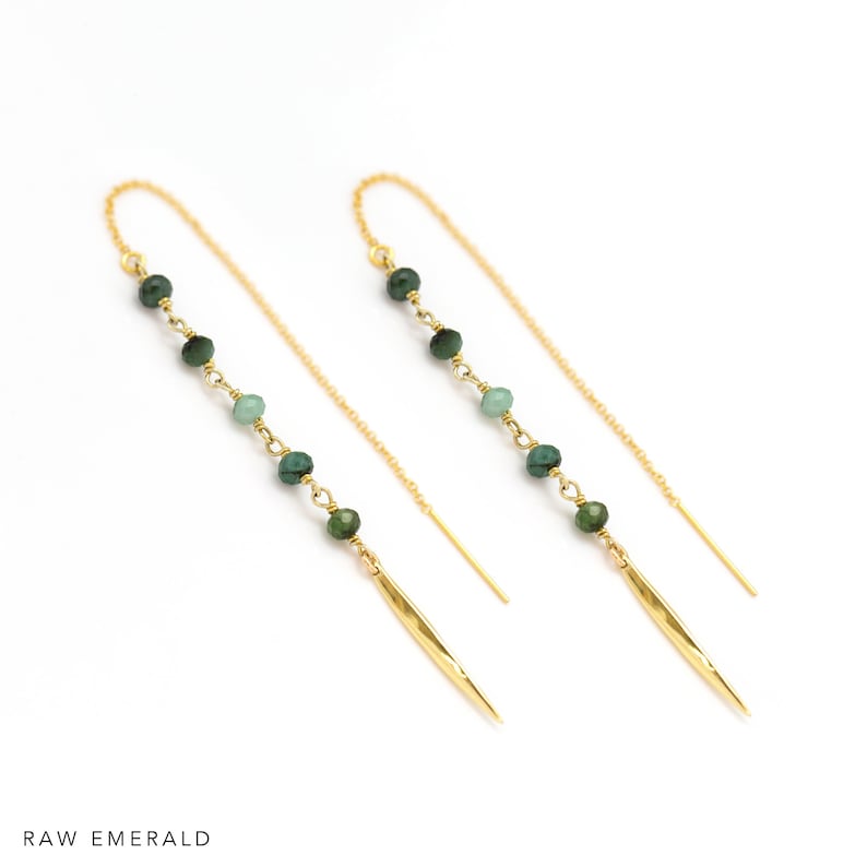 K&ouml;nnte beinhalten: Goldene Ohrh&auml;nger mit gr&uuml;nen Smaragdperlen und einem goldenen Stachelanh&auml;nger. Die Ohrringe werden vor wei&szlig;em Hintergrund gezeigt. Der Text "RAW EMERALD" befindet sich am unteren Bildrand.