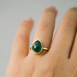 May include: A gold ring with a teardrop-shaped green gemstone.