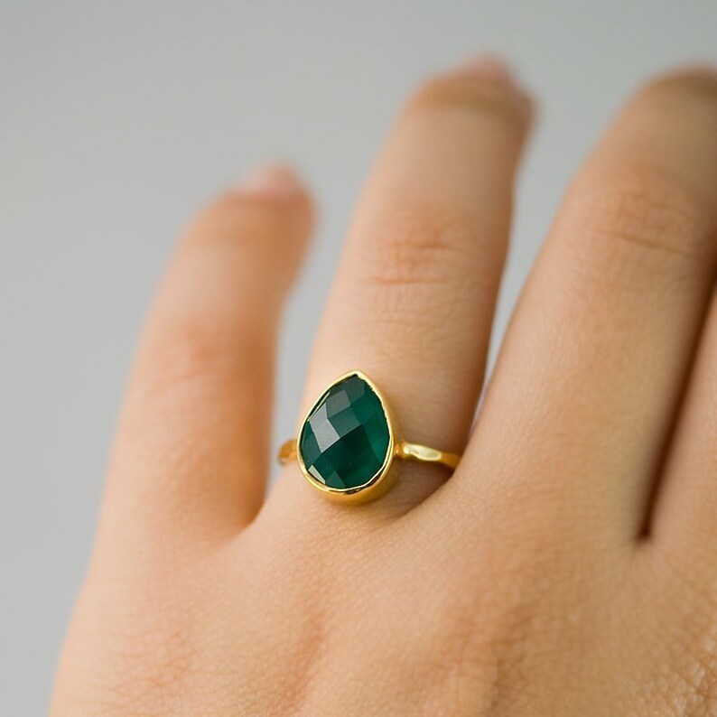 May include: A gold ring with a teardrop-shaped green gemstone.
