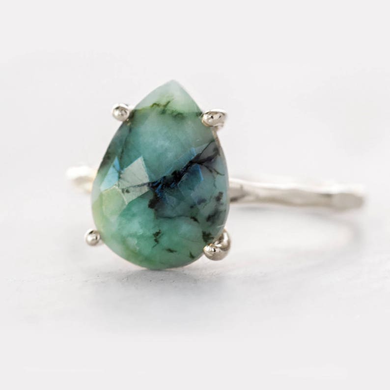 May include: A pear-shaped emerald green gemstone ring with a silver band. The gemstone has a faceted cut and is set in a silver prong setting.