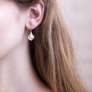 May include: Gold earrings with a delicate, curved design and a single pearl drop.