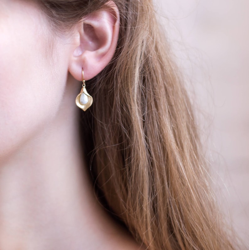 May include: Gold earrings with a delicate, curved design and a single pearl drop.