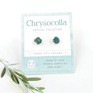 Op de afbeelding: Een paar turquoise chrysocolla-kristallen oorbellen op een witte kaart met de tekst "Chrysocolla Crystal Collection" en "Third Eye Chakra". De kaart bevat ook een symbool van de derde oogchakra en de tekst "Chakra of Vision. Personal Growth and Inner Clarity."