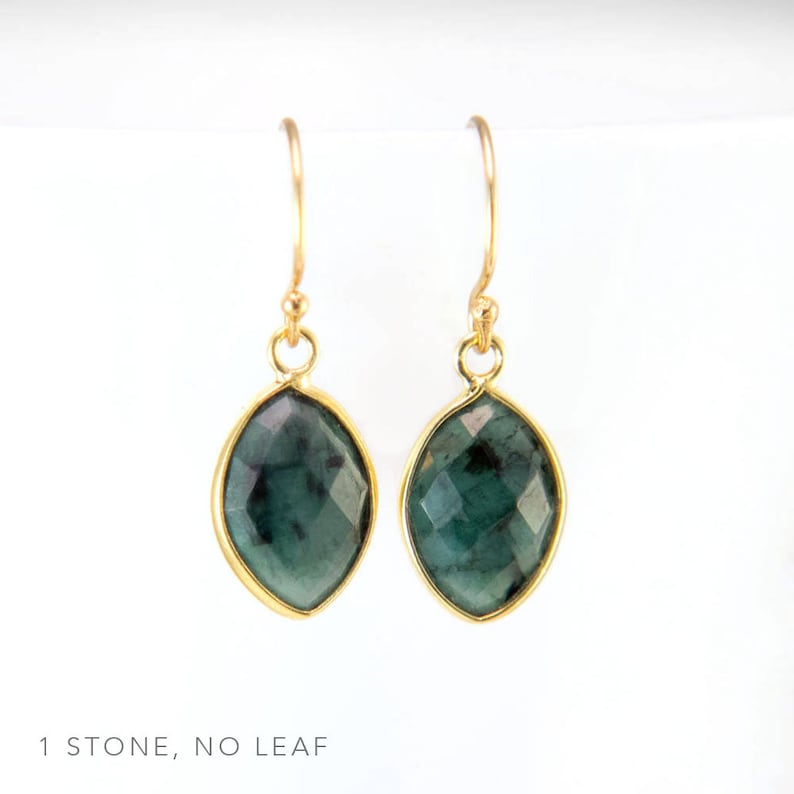 May include: A pair of gold earrings with a single, dark green gemstone in each earring. The gemstones are faceted and have a slightly oval shape.