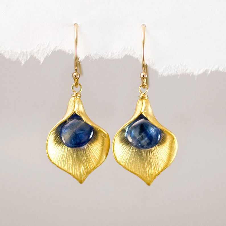 Puede incluir: Pendientes de oro con detalles de piedras preciosas azules. Los pendientes tienen forma de p&eacute;talo de flor.