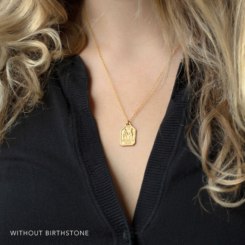 May include: Gold necklace with a zodiac pendant featuring the Gemini symbol. The pendant is a rectangular shape with rounded corners and has a detailed depiction of the Gemini twins.