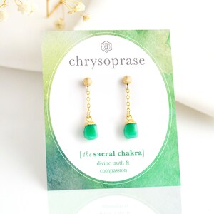 Può includere: Orecchini d'oro con una pietra di crisoprasio verde. Gli orecchini sono etichettati "il chakra sacrale" e "verità divina e compassione".