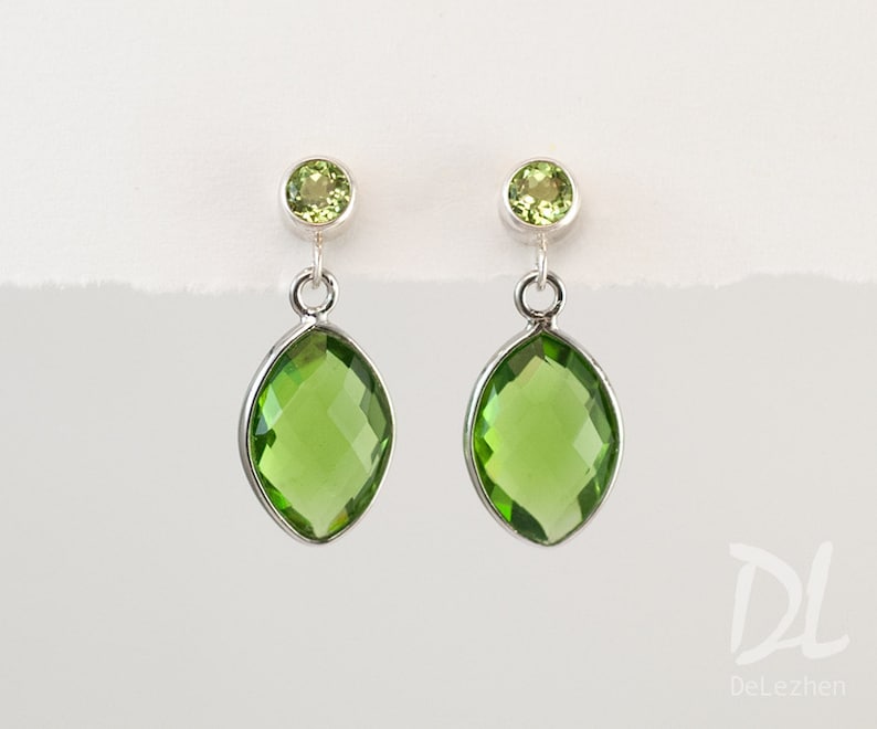 May include: Silver earrings with peridot gemstones. Each earring has a small, round peridot at the top and a larger, marquise-shaped peridot pendant. The gemstones are a vibrant, light green colour.