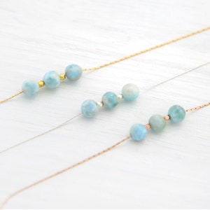 Pu&ograve; includere: Tre delicate collane con perline di pietre preziose blu e bianche su uno sfondo di legno bianco. Le collane sono realizzate con catene in oro, argento e oro rosa.