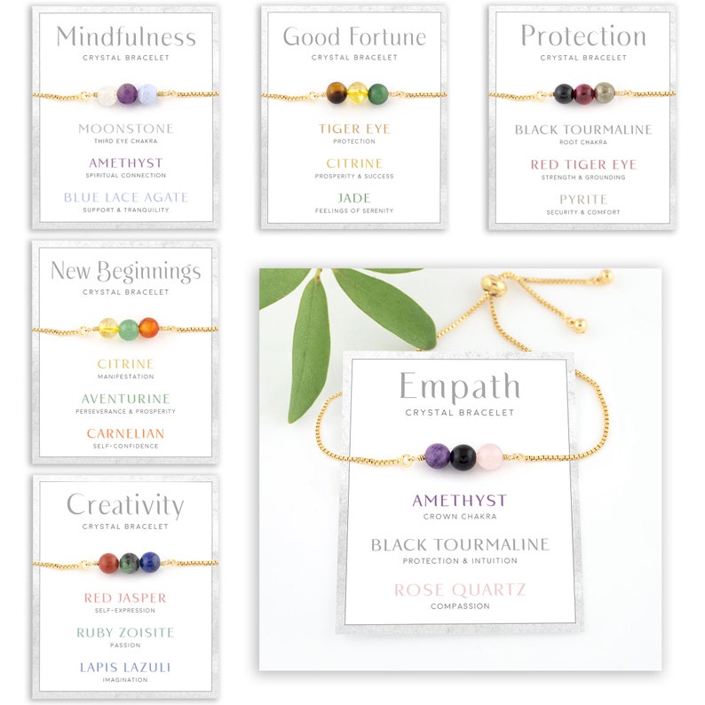 May include: Several crystal bracelets with gold chains and colourful gemstone beads. The bracelets are presented on cards labelled with words like "Mindfulness" and "Good Fortune". The image has a clean, minimalist aesthetic.