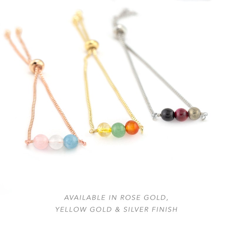 May include: Three adjustable bracelets with colourful gemstone beads. The bracelets are available in rose gold, yellow gold, and silver finishes. The rose gold bracelet has pink, white, and blue beads. The yellow gold bracelet has yellow, green, and orange beads. The silver bracelet has black, red, and gold beads.