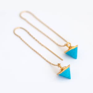 May include: A pair of gold dangle earrings with turquoise triangle-shaped charms.