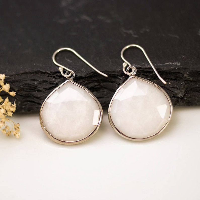 May include: A pair of silver dangle earrings with white teardrop-shaped stones.