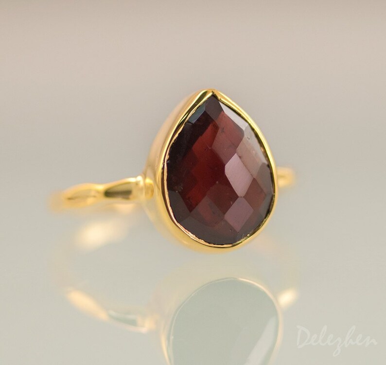 K&ouml;nnte beinhalten: Ein goldener Ring mit einem tropfenf&ouml;rmigen Granat-Edelstein. Der Edelstein ist tiefrot und hat einen facettierten Schliff.