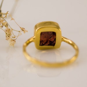 K&ouml;nnte beinhalten: Ein goldener Ring mit einem quadratischen roten Edelstein, der in einer goldenen Fassung sitzt.