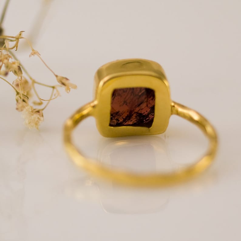 K&ouml;nnte beinhalten: Ein goldener Ring mit einem quadratischen roten Edelstein, der in einer goldenen Fassung sitzt.