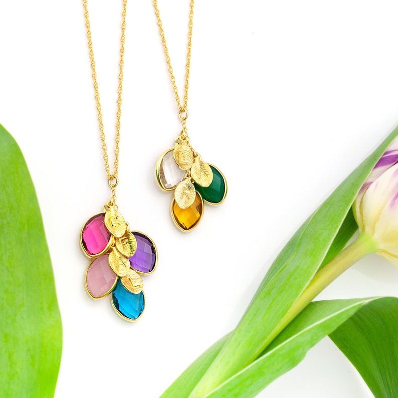 May include: Two gold necklaces with colorful gemstone pendants. The necklaces feature multiple small gold leaves and are displayed against a white background with a green leaf.