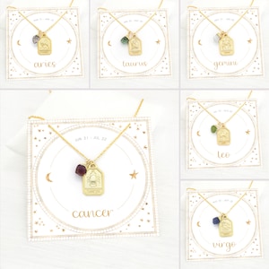 May include: Gold zodiac necklace with a gemstone charm on a white card with gold stars and a crescent moon. The card has the zodiac sign and dates for each sign. The signs shown are Aries, Taurus, Gemini, Cancer, Leo, and Virgo.