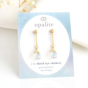May include: Gold earrings with a teardrop-shaped opalite stone. The earrings are on a white card with the text "opalite" and "[the third eye chakra] personal power, love & hope".