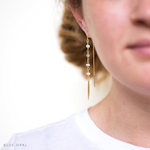 K&ouml;nnte beinhalten: Goldene Ohrringe mit hellblauen Opalperlen und einem goldenen Stachel-Anh&auml;nger. Der Text "BLUE OPAL" ist am unteren Rand des Bildes zu sehen.