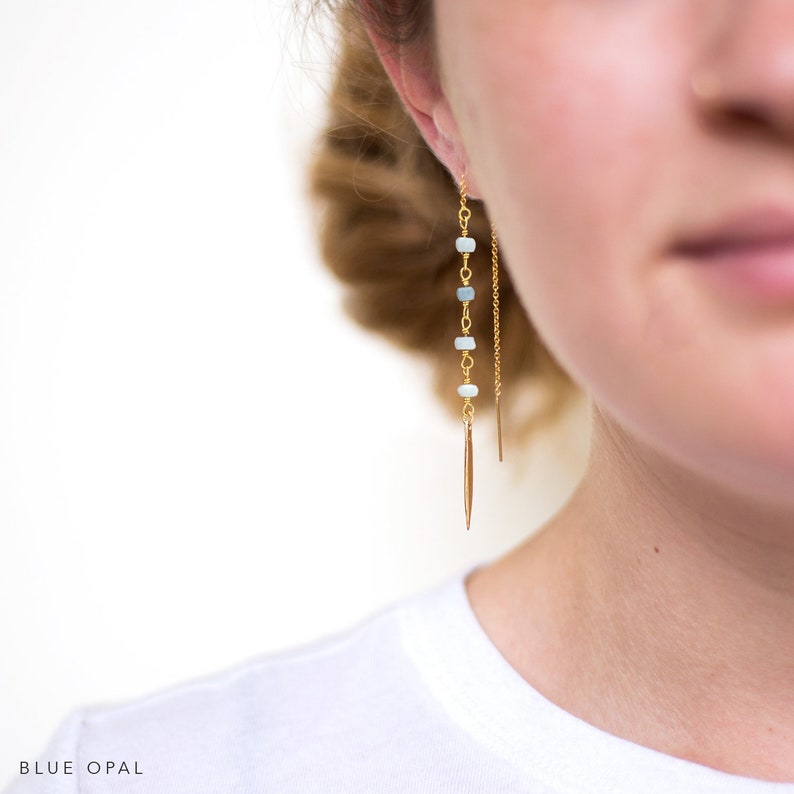 K&ouml;nnte beinhalten: Goldene Ohrringe mit hellblauen Opalperlen und einem goldenen Stachel-Anh&auml;nger. Der Text "BLUE OPAL" ist am unteren Rand des Bildes zu sehen.