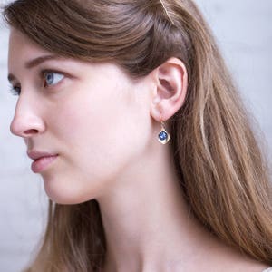 May include: Gold earrings with a blue gemstone set in a delicate, leaf-shaped design.
