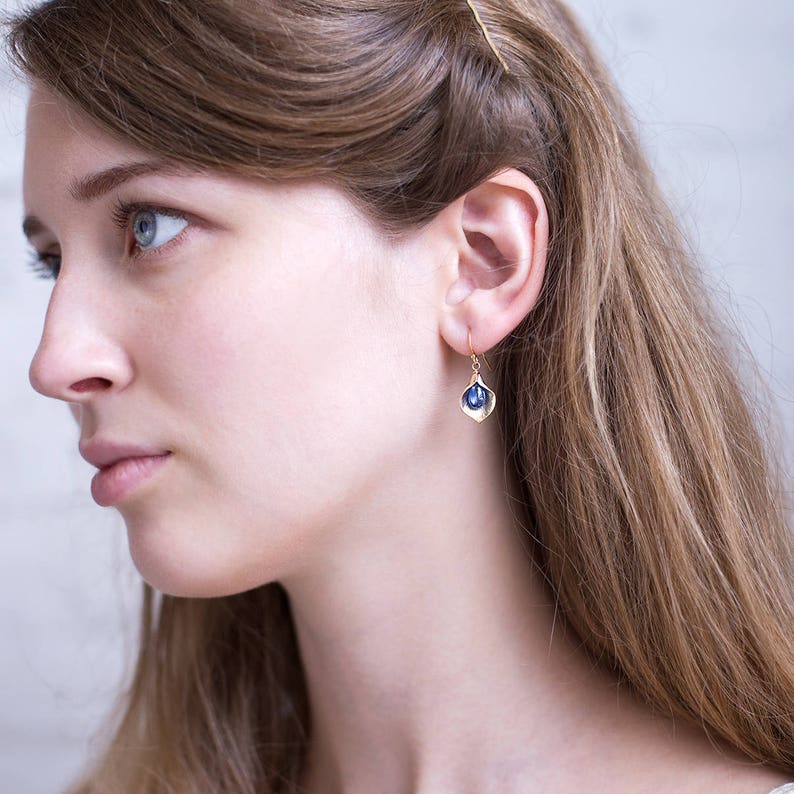 May include: Gold earrings with a blue gemstone set in a delicate, leaf-shaped design.