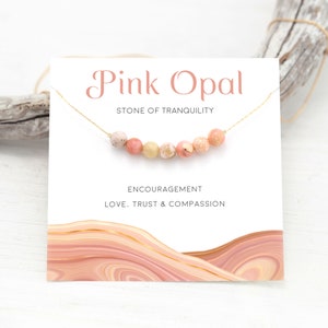 May include: Pink Opal necklace with a gold chain and pink and white beads. The card reads "Pink Opal, Stone of Tranquility, Encouragement, Love, Trust & Compassion".