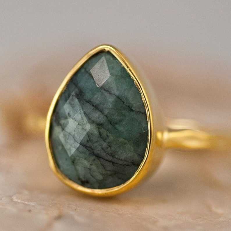 Pode incluir: Um anel de ouro com uma grande gema verde esmeralda em forma de l&aacute;grima.