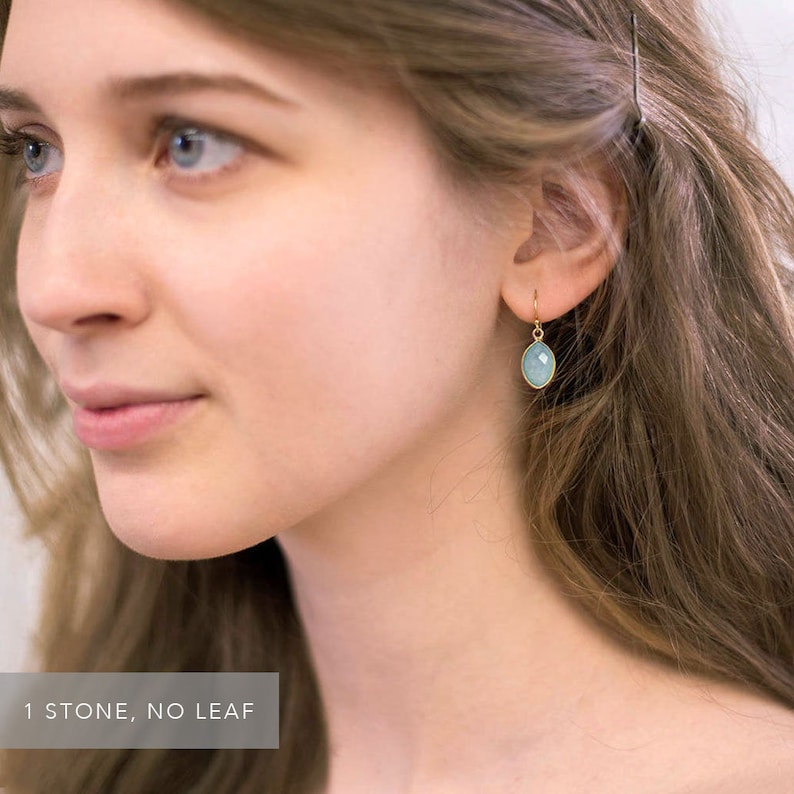 May include: A pair of gold earrings with a single light blue gemstone on each earring. The earrings are simple and elegant.