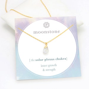 Op de afbeelding: Een gouden ketting met een klein, traanvormig hangertje van maansteen. De kaart staat erbij: "moonstone [the solar plexus chakra] inner growth & strength".
