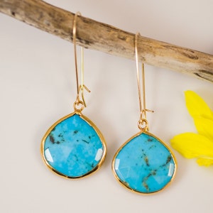 May include: A pair of gold dangle earrings with turquoise teardrop-shaped stones. The stones have a marbled pattern and are set in a gold bezel.
