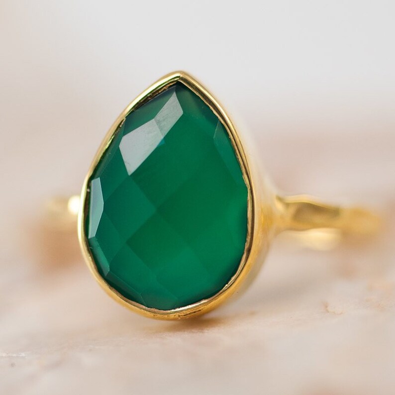 May include: A gold ring with a large, faceted, teardrop-shaped green gemstone.