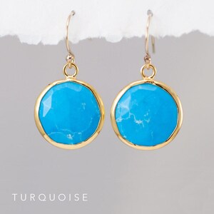May include: A pair of gold earrings with turquoise stones. The stones are round and have a slightly irregular shape. The earrings are simple and elegant.