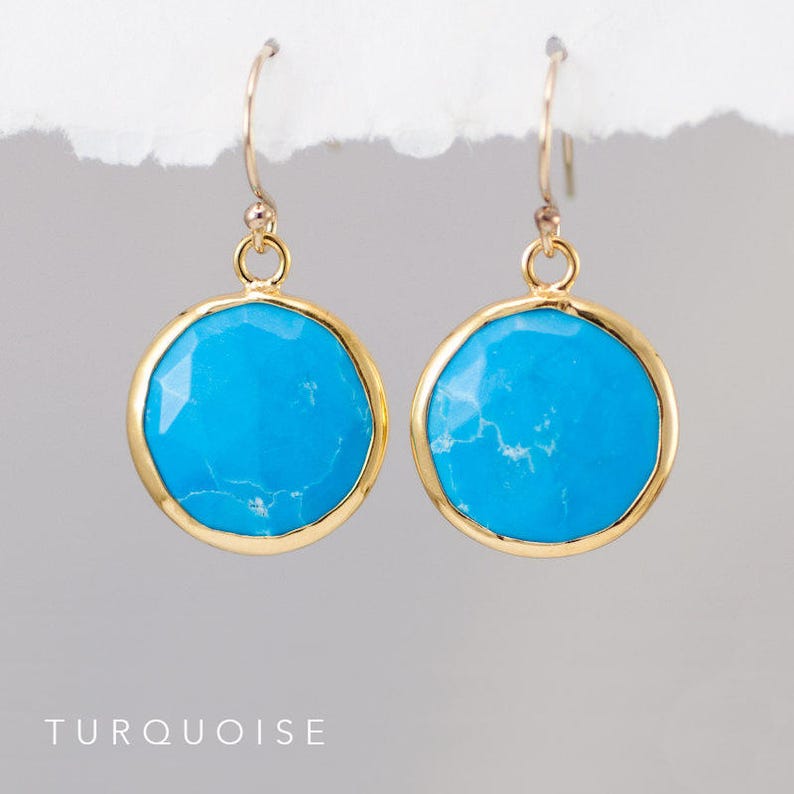 May include: A pair of gold earrings with turquoise stones. The stones are round and have a slightly irregular shape. The earrings are simple and elegant.