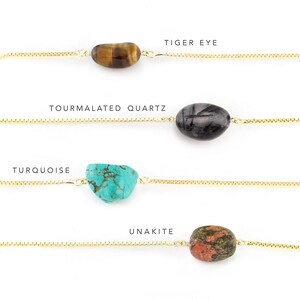 May include: Four gold chain bracelets with different gemstone charms. The charms are tiger eye, tourmaline quartz, turquoise, and unakite.