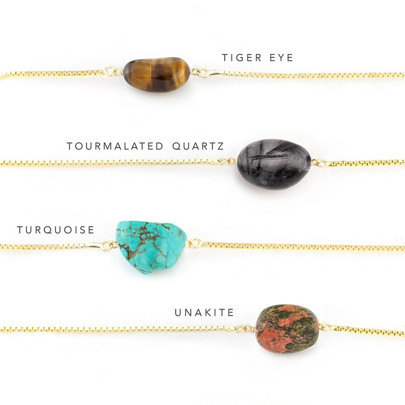 May include: Four gold chain bracelets with different gemstone charms. The charms are tiger eye, tourmaline quartz, turquoise, and unakite.