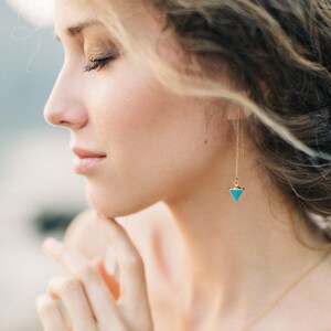 May include: A woman wearing a pair of gold dangle earrings with turquoise triangle-shaped stones.