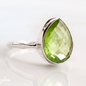 May include: A silver ring with a large, faceted, pear-shaped green gemstone.