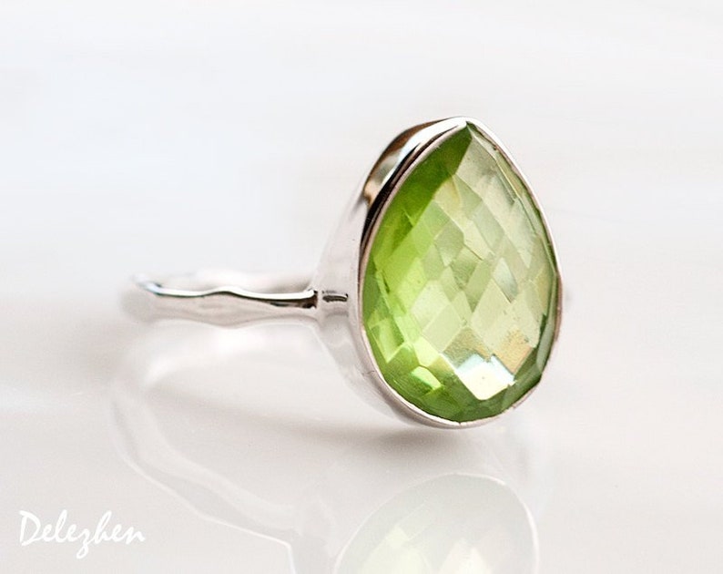 May include: A silver ring with a large, faceted, pear-shaped green gemstone.