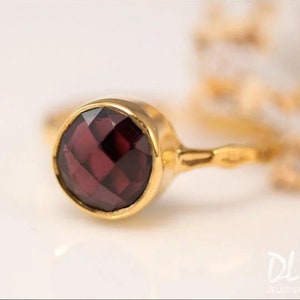 May include: A gold ring with a dark red gemstone. The ring has a simple, delicate design.