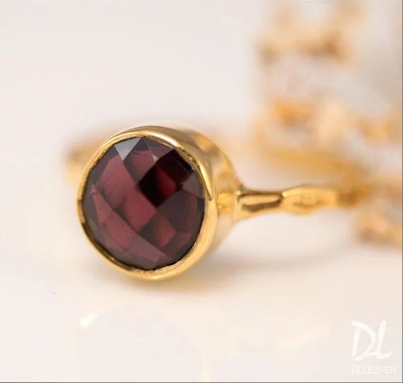 May include: A gold ring with a dark red gemstone. The ring has a simple, delicate design.