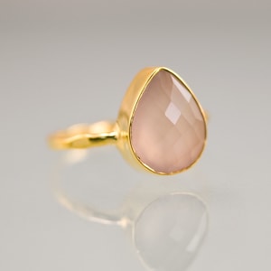 K&ouml;nnte beinhalten: Ein goldener Ring mit einem tropfenf&ouml;rmigen, facettierten, hellrosa Edelstein. Der Ring hat ein schlichtes, elegantes Design mit einem glatten, polierten Goldband. Der Edelstein ist in einer goldenen L&uuml;nette gefasst.