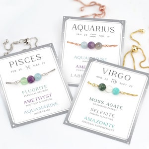 May include: Three zodiac-themed bracelets with gemstone beads. The bracelets are on cards with the zodiac sign, dates, and the name of the gemstone and its meaning. The bracelets are silver, gold, and rose gold.